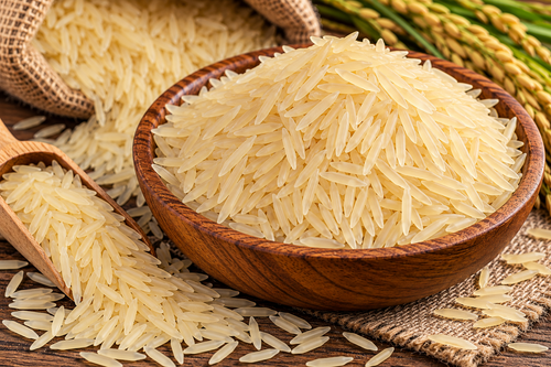 Golden long grain parboiled sella rice in a wooden bowl with loose grains and a wooden scoop